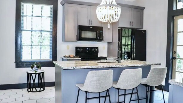 A modern kitchen with a central island, bar stools, a microwave, a refrigerator, and a chandelier. - Walk to Downtown Monroe- The Blue Daisy Cottage (Monroe)