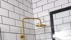 A corner shower with white tiled walls and a gold showerhead. - Walk to Downtown Monroe- The Blue Daisy Cottage (Monroe)