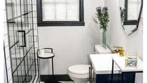 A bathroom with a black and white tiled floor, a toilet, a sink with a mirror, and a window with blinds. - Walk to Downtown Monroe- The Blue Daisy Cottage (Monroe)