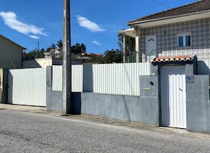 Una proprietà recintata con una staccionata in lamiera ondulata, un portone bianco e un tetto in tegole.