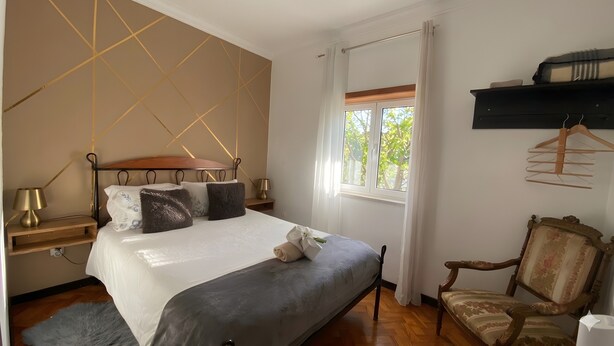 A bedroom with a bed, bedside tables, a chair, a window, and a hanging clothes rack. - Apartment 'Alojamento D Duarte T1' with Mountain View, Balcony and Wi-Fi (Gouveia)