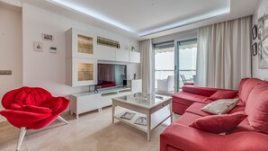 Una sala de estar moderna con un sofá rojo, una mesa de centro de cristal, una butaca roja y un mueble blanco para el equipo de entretenimiento.