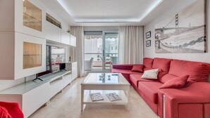 Una sala de estar moderna con una mesa de centro de vidrio, sofá rojo y un ventanal con vista a un puente.