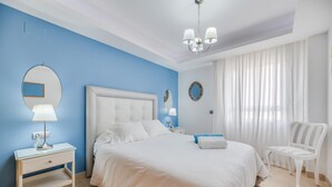 Un dormitorio con una cama, una mesita de noche, una silla, un espejo y una ventana con cortinas.