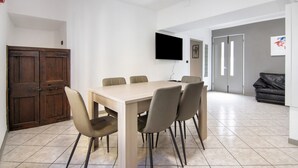 A dining area with a wooden table and six chairs, a television mounted on the wall, and a dark leather sofa in the background. - Holiday Apartment "Dongo Garden" with Private Garden & Wi-Fi (Dongo)