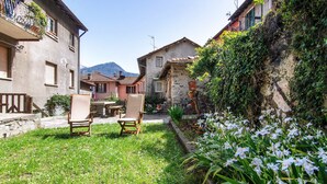 A courtyard with outdoor seating, a stone wall with vegetation, and a mountain in the background. - Holiday Apartment "Dongo Garden" with Private Garden & Wi-Fi (Dongo)