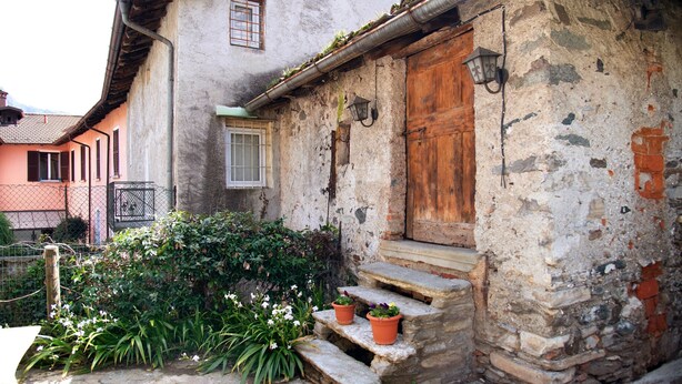 A rustic building with a wooden door, stone steps, and a small garden with potted plants. - Holiday Apartment "Dongo Garden" with Private Garden & Wi-Fi (Dongo)