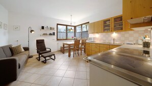 A modern kitchen with wooden cabinets, a dining area with a table and chairs, and a living area with a sofa and a lamp.