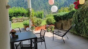 A patio with a table and chairs, surrounded by potted plants and a view of a forested area.