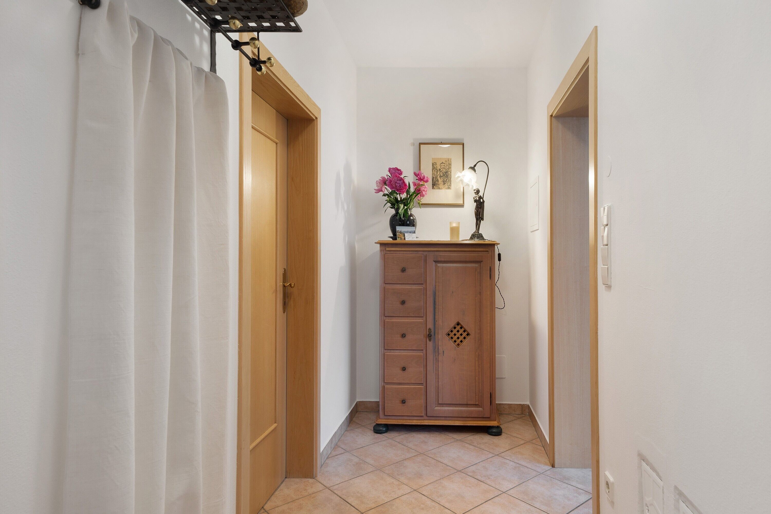 A narrow hallway with a wooden cabinet, a framed picture, and a vase with flowers.