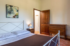 A bedroom with a bed, a nightstand, a dresser, a wooden door, and a painting on the wall.