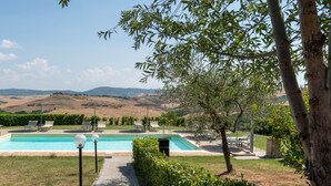 Une piscine entourée de chaises longues et accessible par un chemin, le tout bordé de verdure et avec des collines en arrière-plan.