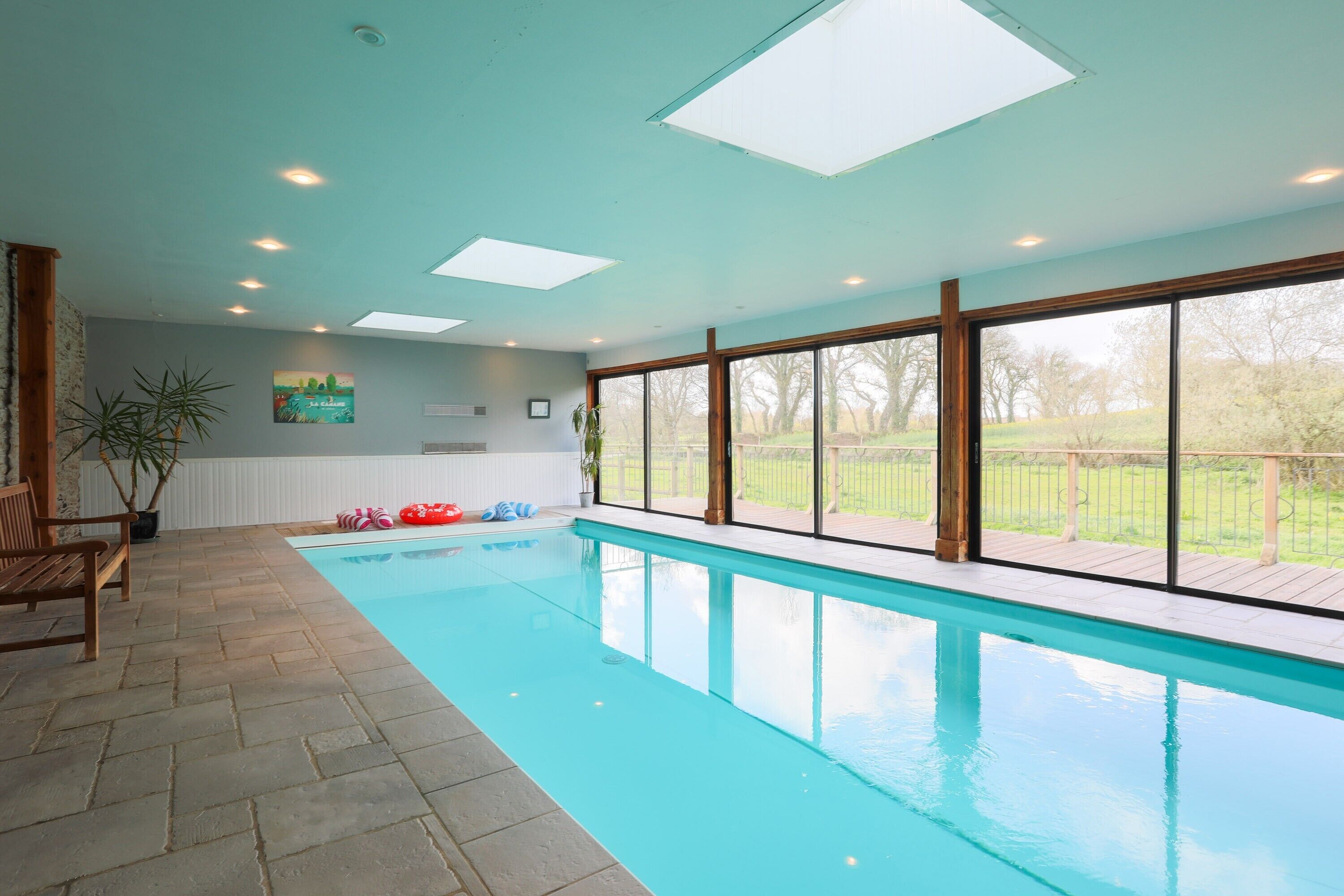 A swimming pool with clear blue water, large windows, and a wooden deck.