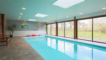 A swimming pool with clear blue water, large windows, and a wooden deck.