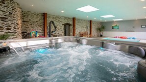 Ein Wellnessbereich mit Whirlpool und einem kleinen Pool, Steinwänden und einem Oberlicht.