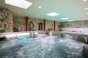 Un área de spa con un jacuzzi y una piscina más pequeña, paredes de piedra y un tragaluz.