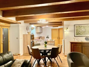 Zona pranzo con tavolo rotondo e sedie, cucina sullo sfondo, travi in legno al soffitto e una mappa incorniciata al muro.