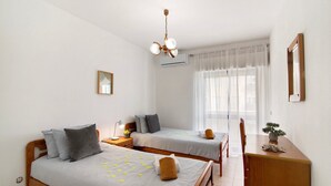 Hotellihuone, jossa on kaksi sänkyä, työpöytä, tuoli, pieni pöytä, jossa on kasvi, ja kattotuuletin.