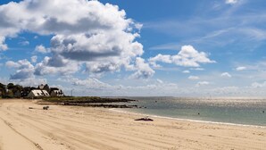 Uma praia com areal, alguns edifícios e céu claro.