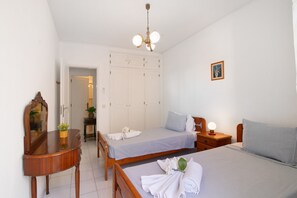 Una camera da letto con due letti, una cassettiera in legno, uno specchio, un ventilatore a soffitto e un armadio.