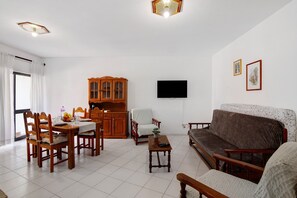 Ein Wohnzimmer mit Esstisch, Stühlen, einer Couch, einem Fernseher und einem Schrank.