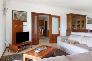 Een woonkamer met een televisie op een houten standaard, een bank, een salontafel en een kast met glazen deuren.