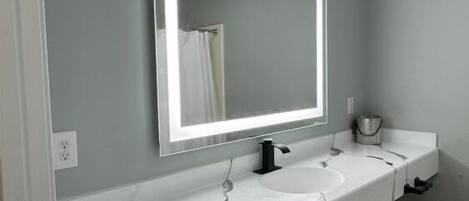 A bathroom with a white vanity, a mirror with backlighting, and a shower curtain.