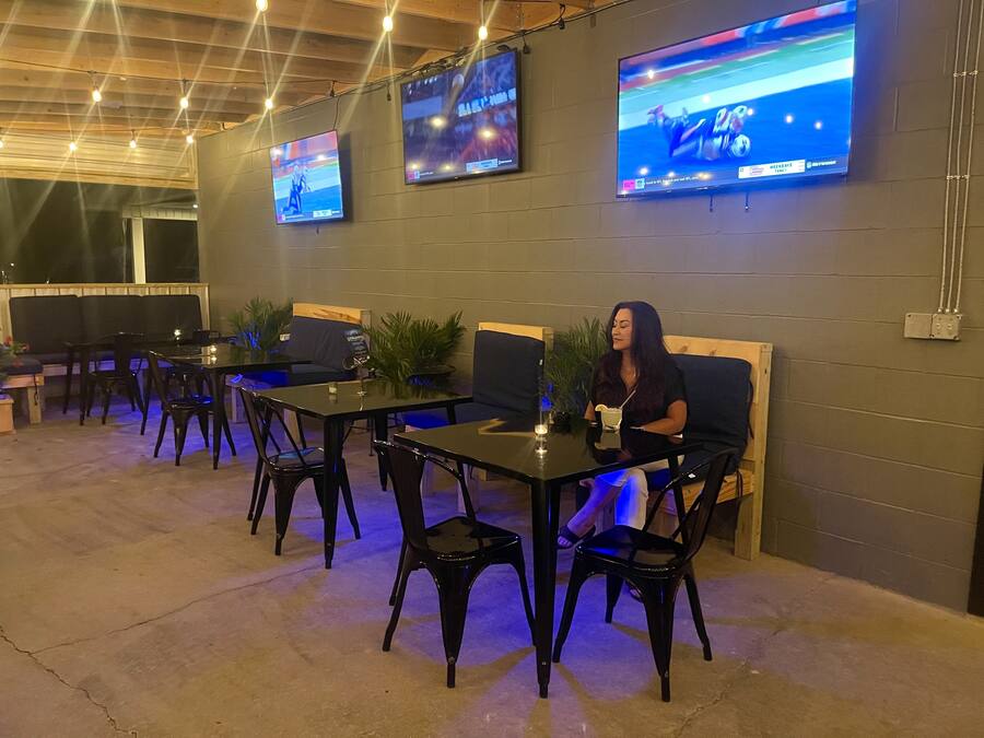 Un espace extérieur aménagé avec des tables et des chaises, un téléviseur fixé au mur et des guirlandes lumineuses suspendues au plafond.