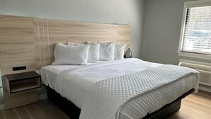 Une chambre à coucher moderne avec une tête de lit en bois, une couvre-lit blanche et une table de chevet.