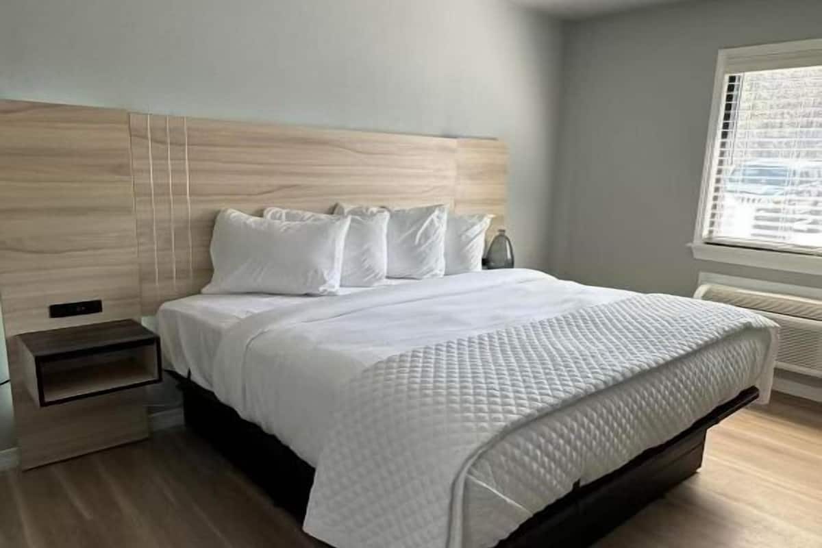 A modern bedroom with a wooden headboard, a white bedspread, and a bedside table.