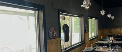A restaurant interior with large windows, wooden walls, and modern pendant lighting.