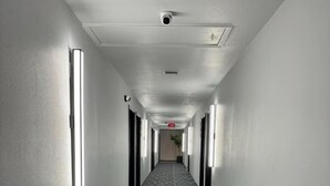 Un long couloir étroit d’hôtel, avec un tapis à motifs, un éclairage au plafond et une caméra de surveillance.