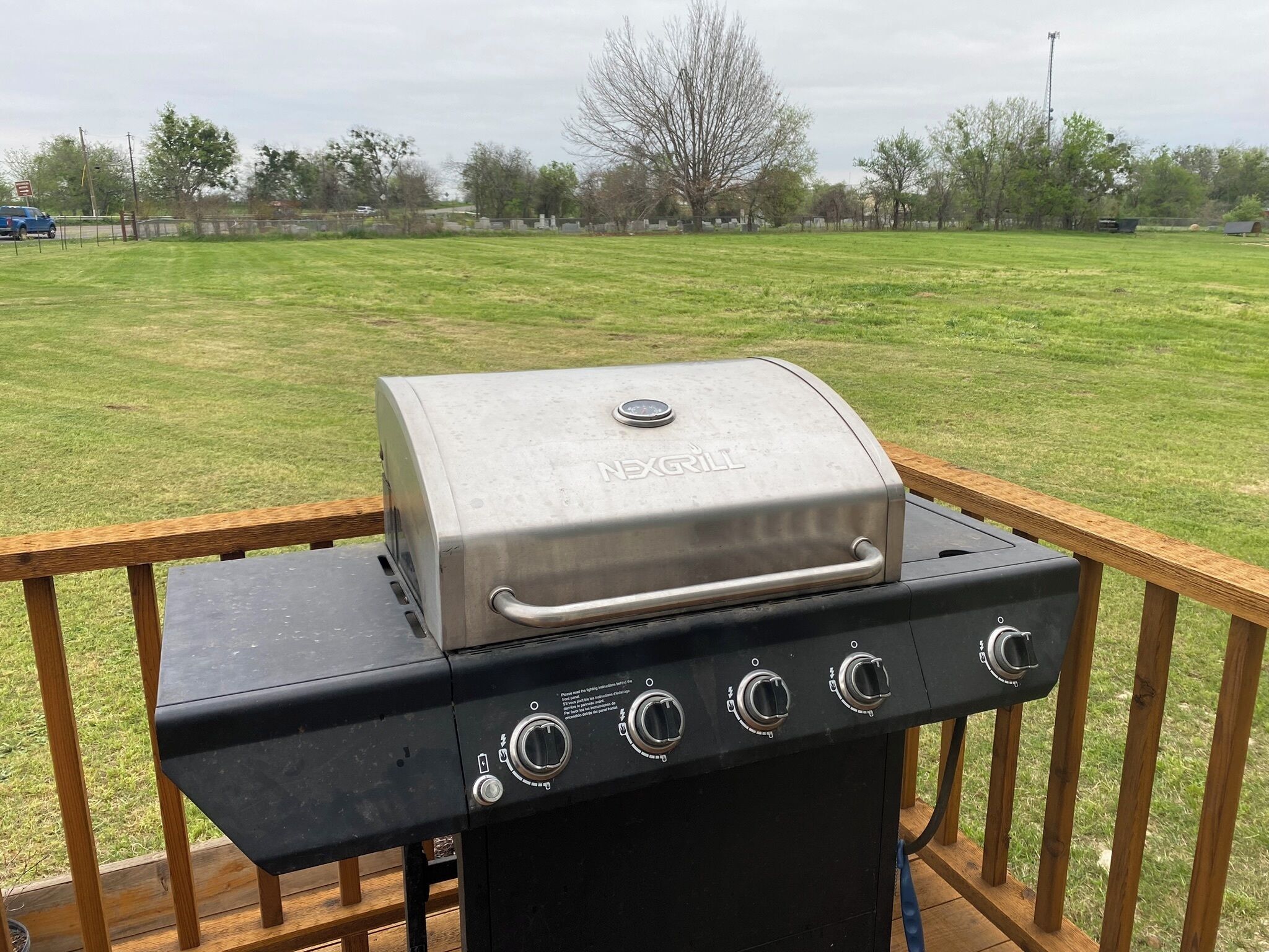 A barbecue grill on an outdoor deck with a view of a grassy field.