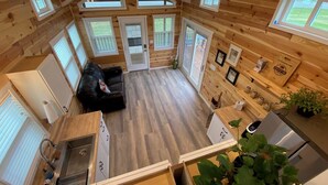 A cozy cabin with a loft bedroom, a living area with a black leather sofa, a kitchen with wooden cabinets, and a dining area with a table and chairs. - Rustic Tiny Home Escape - Pets Stay Free! (Georgetown)