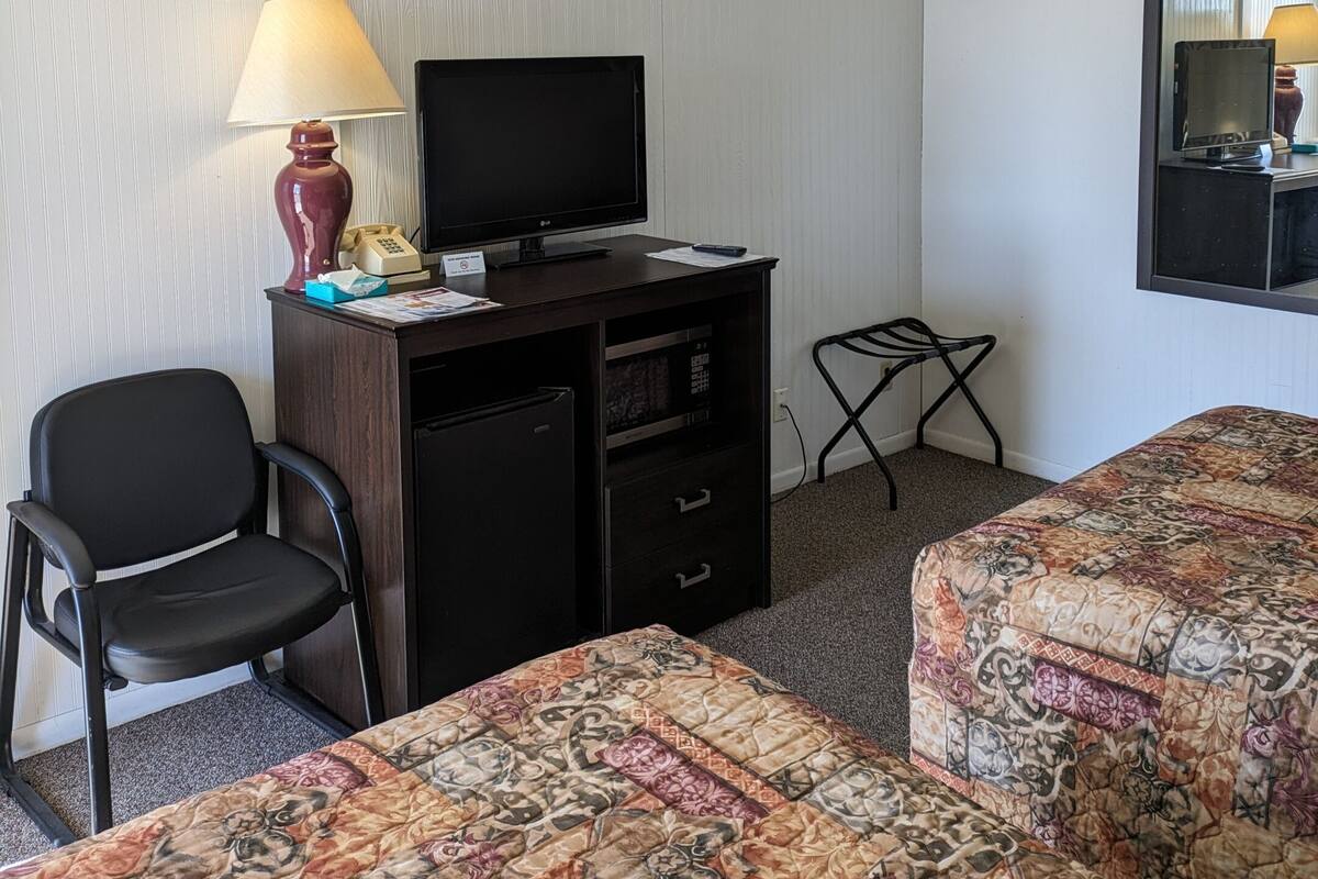 Une chambre d’hôtel équipée d’un bureau, d’une chaise, d’une télévision, d’un lit et d’une petite table avec une lampe.