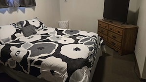 Een slaapkamer met een bed, een dressoir, een televisie en een raam met gordijnen.