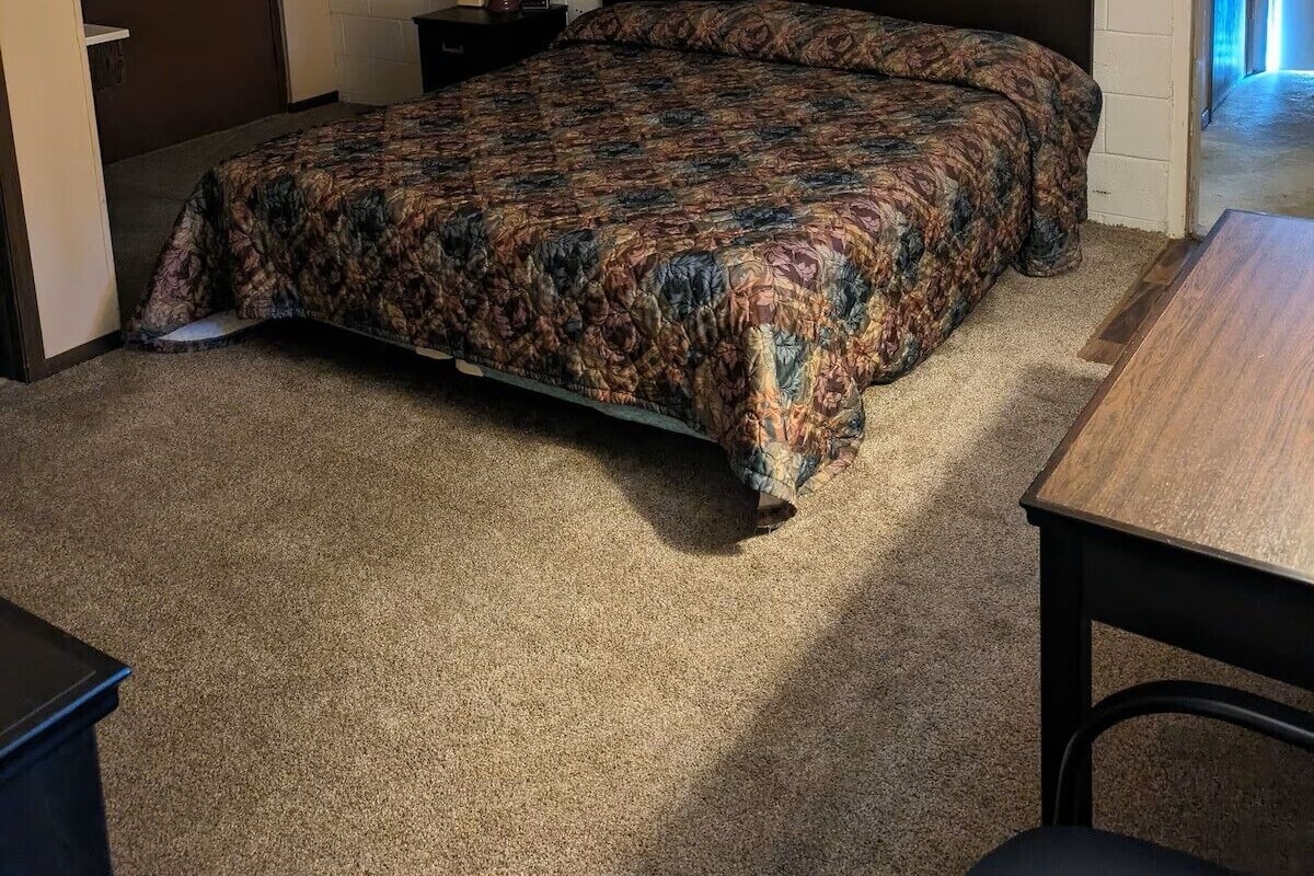 Une chambre à coucher avec un lit, une table de chevet, une lampe, un tableau encadré au mur et une porte.