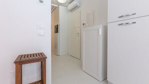 A narrow hallway with a white refrigerator, a wooden side table, and a door leading to another room. - GuestHost - Academy of Fine Arts -Modern Apt. with balcony! (Bologna)