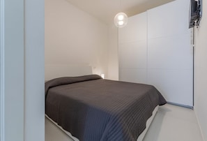 A bedroom with a bed, a wall-mounted TV, and a ceiling light fixture.