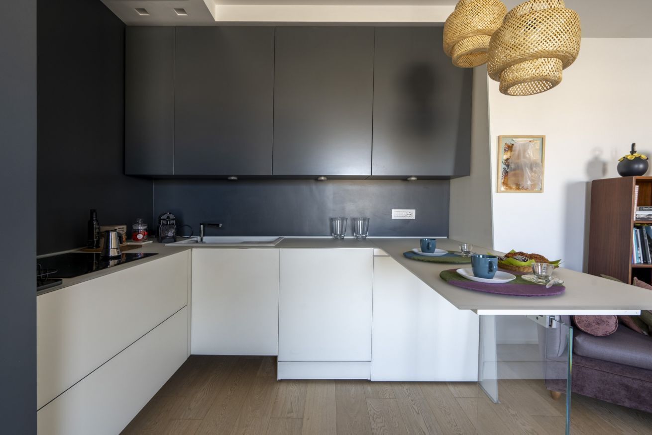 Una cocina moderna con armarios oscuros, encimera blanca y zona de comedor con mesa y sillas.