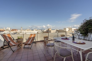 Eine Dachterrasse mit Esstisch, Liegestühlen und Blick auf die Stadt.