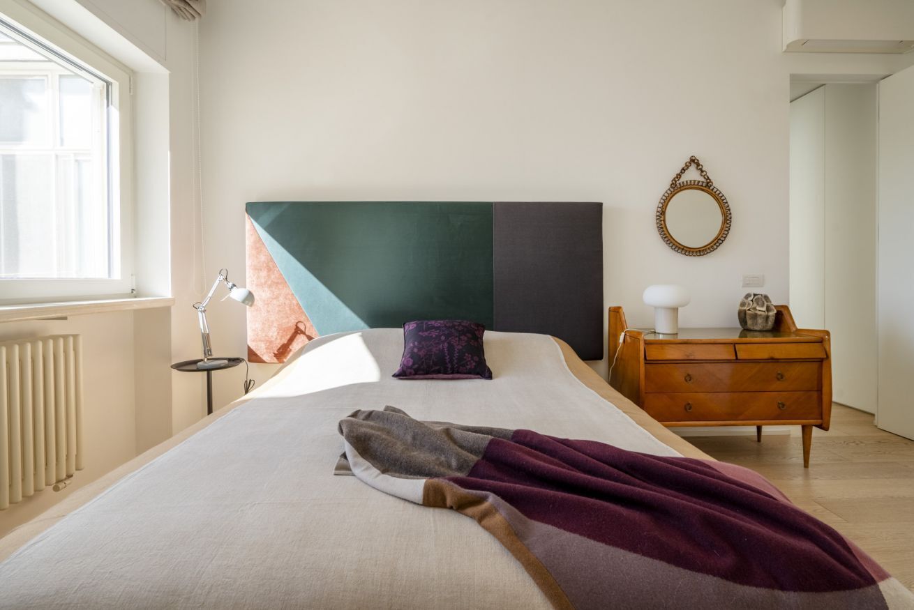A bedroom with a bed, a dresser, a mirror, and a window.