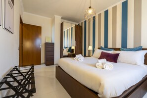 Una habitación de hotel con una cama, una puerta de madera, un aparador, un espejo y una lámpara colgante.
