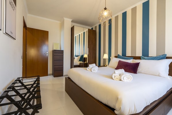 A hotel room with a bed, a wooden door, a dresser, a mirror, and a hanging light fixture.