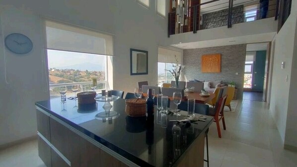 A modern kitchen with a central island, dining area with chairs, and a view of the outdoors.