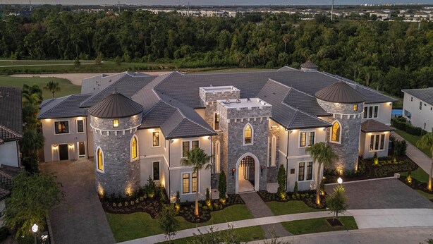 A large, multi-story house with a stone facade, multiple towers, and a well-maintained lawn.