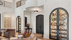 A spacious lobby with a checkered floor, a seating area with sofas, a wine rack, and a large black door.