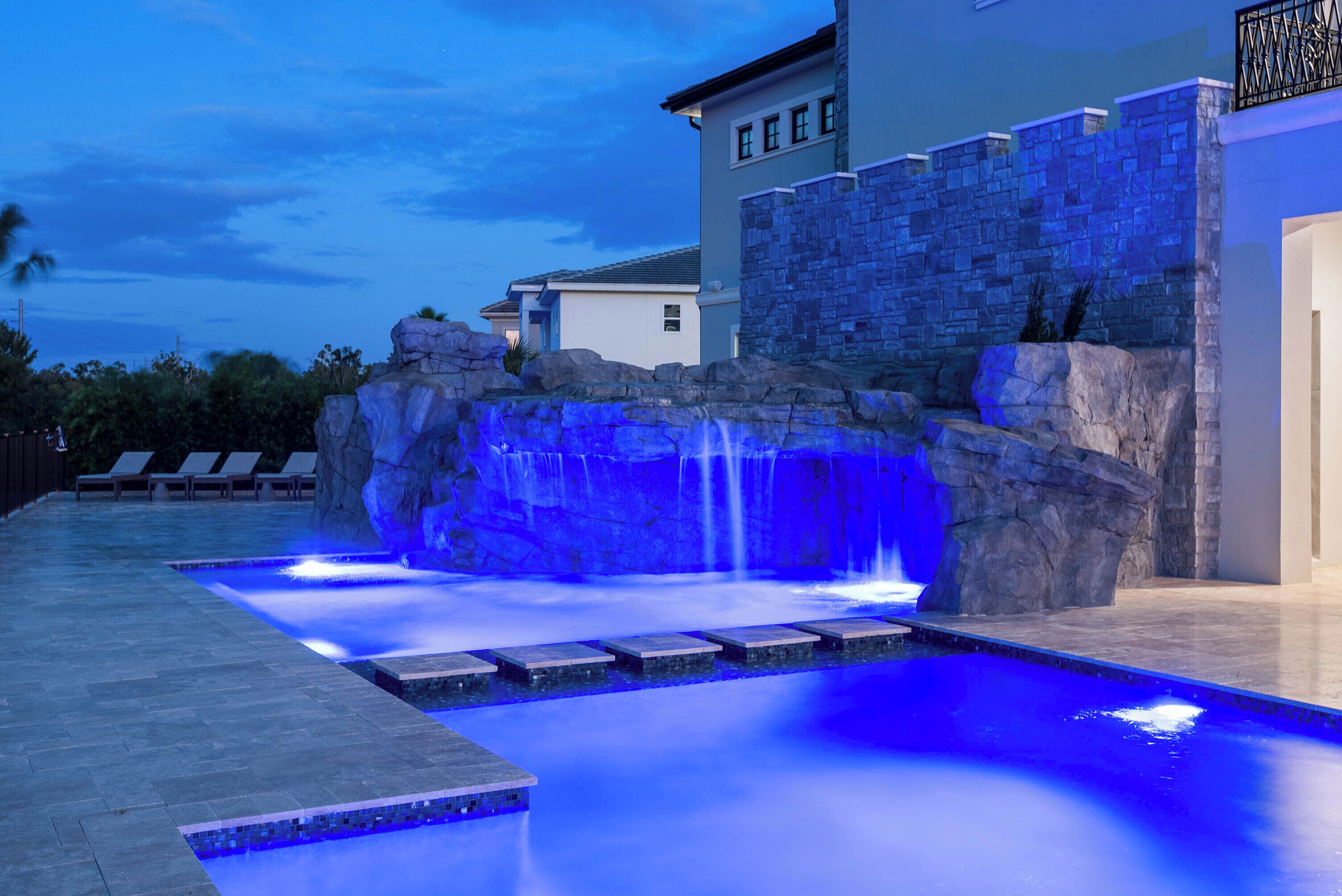 Una piscina con cascata, pareti in pietra e poltrone relax.