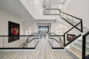 Ein modernes Interieur mit einer Glas-Geländer-Treppe, einem großen gerahmten Kunstwerk an der Wand und Blick in einen Wohnbereich.