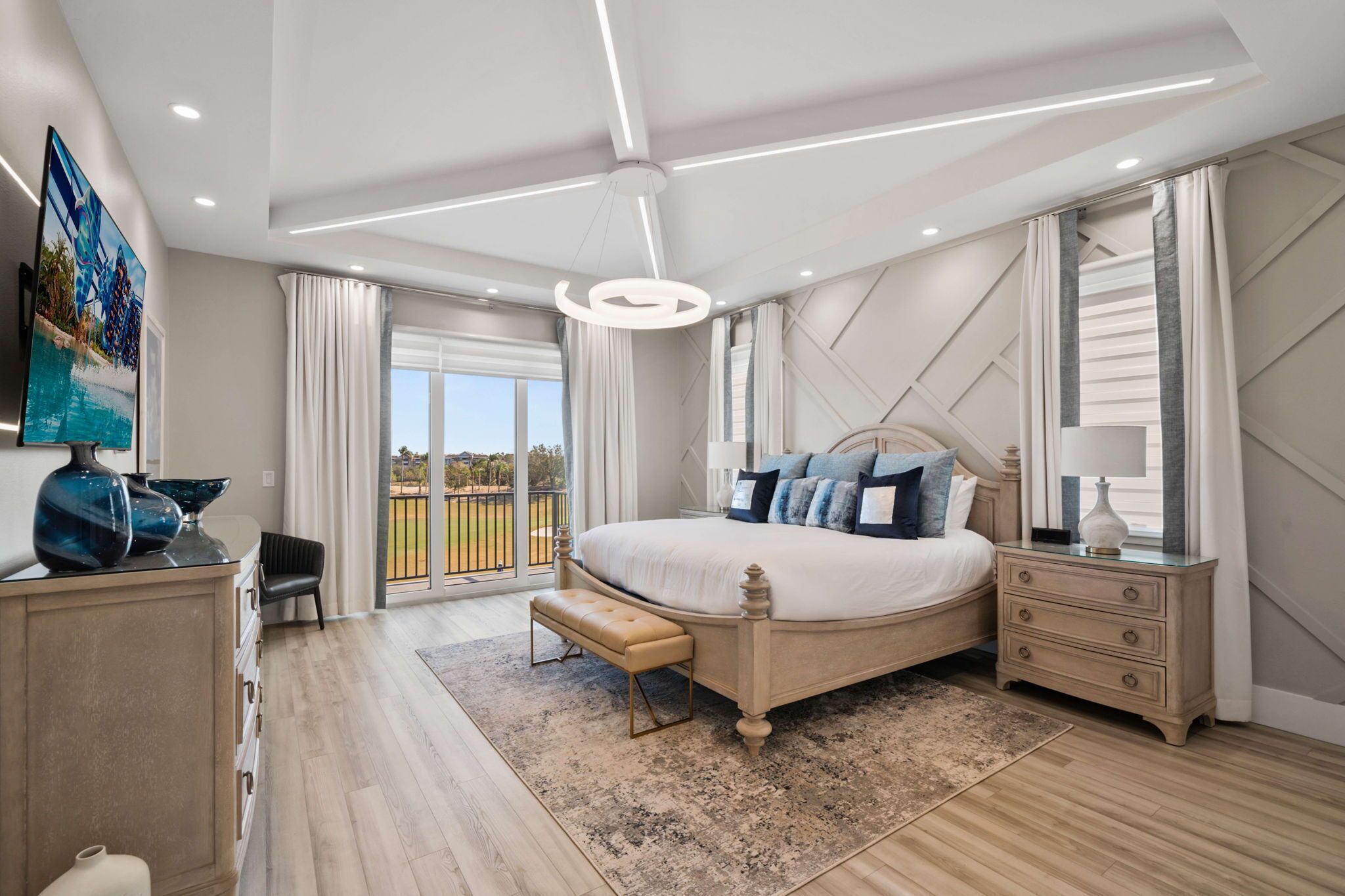 A modern bedroom with a large bed, a bedside table, a bench, and a view of the outdoors.